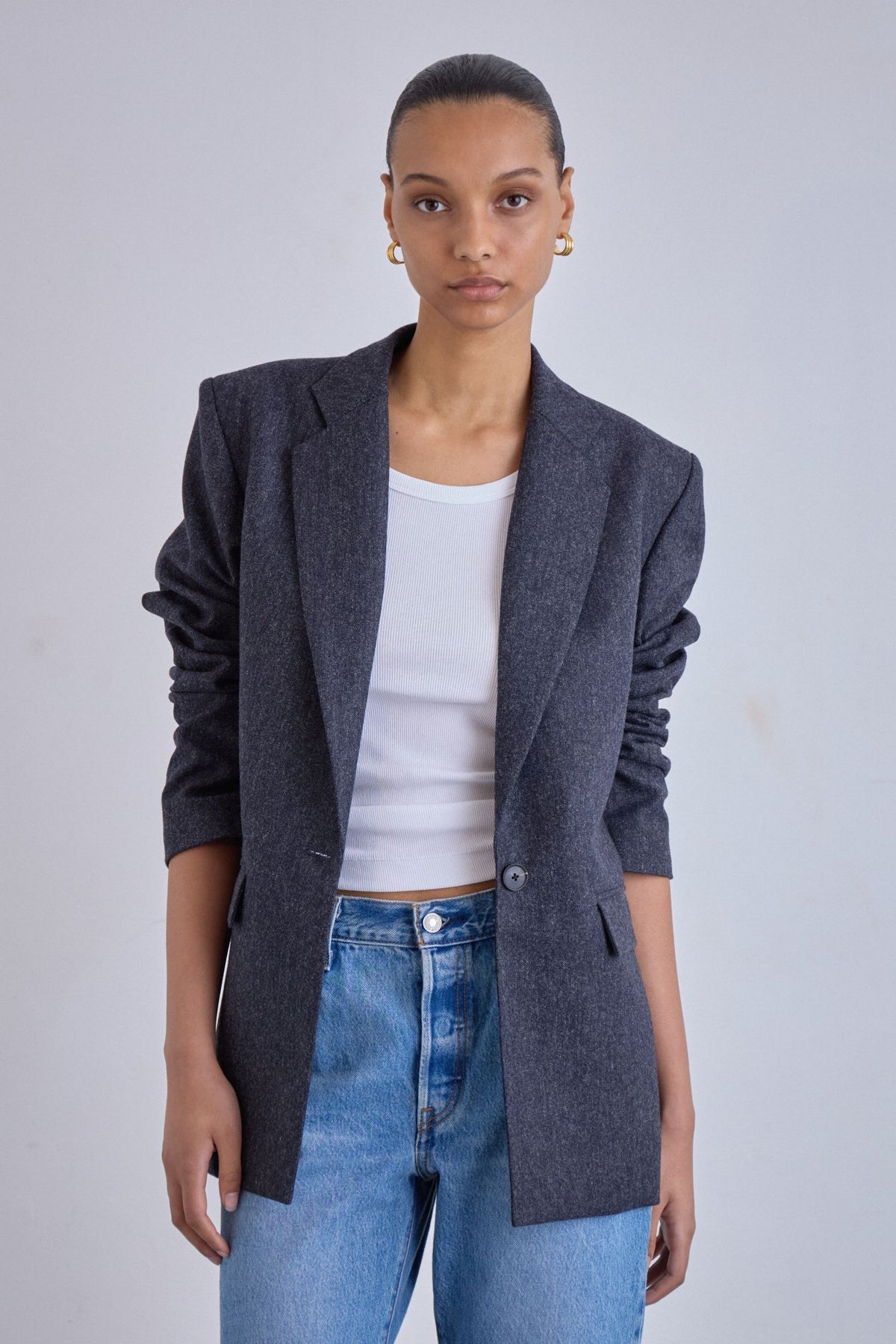 Person wearing a gray blazer over a white top and blue jeans on a plain background